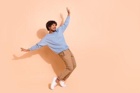 Full body photo of carefree guy wear blue shirt trousers stand on tiptoes look at sale empty space isolated on beige color backgroundの写真素材