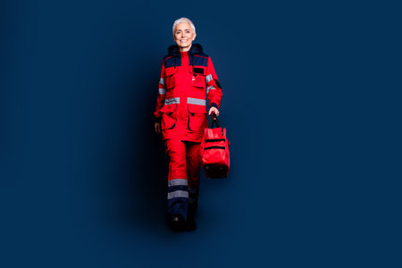 Full length photo of lovely pensioner lady provide emergency medical help walk dressed red uniform isolated on dark blue color backgroundの写真素材