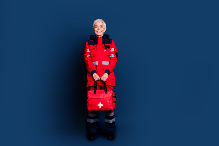 Full size photo of pretty retired female ambulance doctor specialist first aid kit.wear red uniform isolated on dark blue color backgroundの写真素材