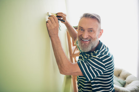 Elderly man enjoying a relaxing weekend at home painting, smiling in casual t-shirt indoors, capturing joyful moments in natural daylightの写真素材