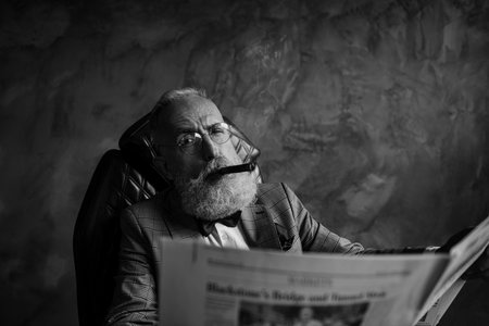 Handsome, attractive rich old man in glasses with cigarette in mouth, hold newspaper, looking at...