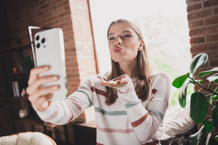 Young woman with blond hair sending kiss during selfie for social mediaの写真素材