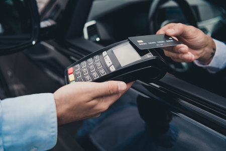 Businessman making contactless payment with card on wireless terminal by parked car outside on city streetの写真素材