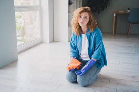 Full body photo of nice ginger young girl tired wipe floor depressed wear blue clothes enjoy modern cozy interior flat indoorsの写真素材