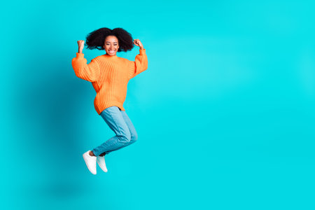 Full length photo of lovely young lady jumping winning dressed stylish knitted orange garment isolated on aquamarine color backgroundの写真素材