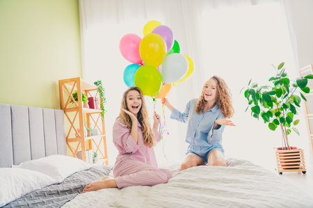 Full size photo of two young women excited receive birthday balloons dressed sleepwear outfit wake up cozy day light bedroom home interiorの写真素材