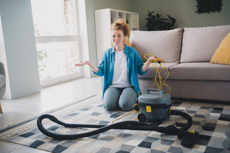 Full size photo of young ginger woman stressed repair vacuum cleaner confused dressed blue outfit cozy day light home interior living roomの写真素材