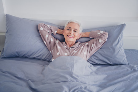 Senior woman waking up happily in cozy bedroom with natural lightの写真素材