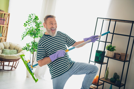 Elderly man enjoying a fun and carefree day at home with a mop as a guitarの写真素材