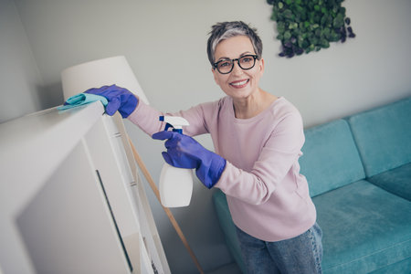 Photo of adorable sweet lady wear pink sweatshirt doing daily cleaning furniture indoors room home...