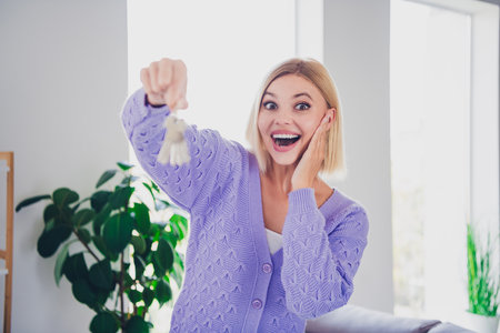Joyful young woman indoors with keys in purple sweater, expressing happiness and comfort