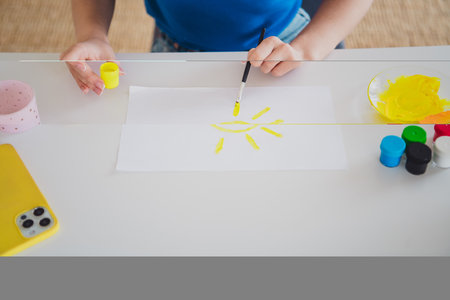 Cropped photo of blonde teenager woman drawing sun paper paint enjoy hobby dressed blue outfit cozy day light home interior living roomの写真素材