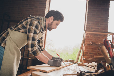 Photo of wood worker guy writing with pencil measure ruler plank in garage indoorsの写真素材