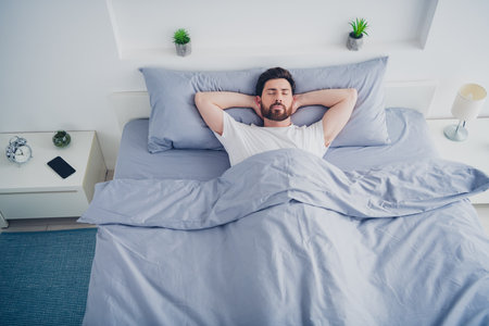 Top view photo of handsome good mood mature guy dressed sleepwear lying bed arms behind head indoors room home houseの写真素材
