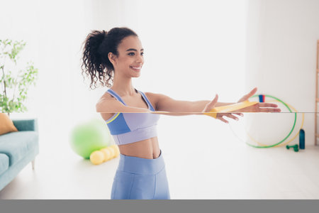 Energetic woman enjoying fitness training at home with resistance bands, showcasing activewear in a...