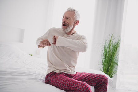 Elderly man in pajamas waking up feeling refreshed and relaxed in a bright bedroomの写真素材