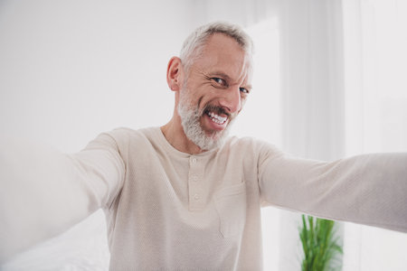 Elderly man in cozy pajamas smiling warmly in bright bedroom