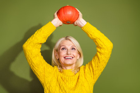 Photo of cheerful pensioner wear yellow clothes arm above head hold ripe pumpkin isolated on green color backgroundの写真素材