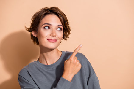 Photo portrait of lovely young lady look point empty space wear trendy gray garment isolated on beige color backgroundの写真素材
