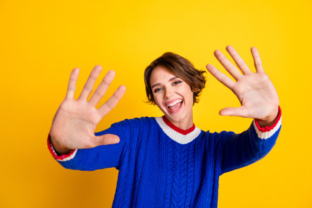 Photo of cheerful positive girl wear blue pullover smiling waving arms hello isolated yellow color...
