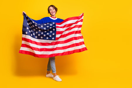 Full length photo of funky excited girl wear blue pullover enjoying american independence day empty space isolated yellow color backgroundの写真素材