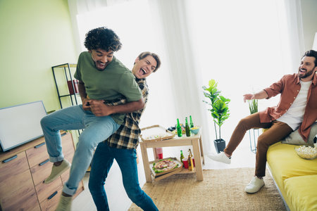 Photo of company three friends fight arms hold throw hang out weekend modern interior apartment indoorsの写真素材