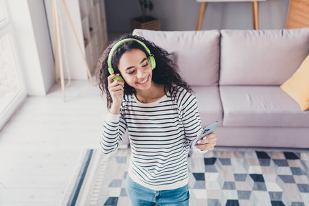 Above view photo of nice young girl headphones smart phone wear striped pullover living room apartment indoorsの写真素材