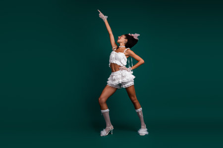 Young woman in elegant white costume posing against a deep green background, exuding charm and playfulness.の写真素材