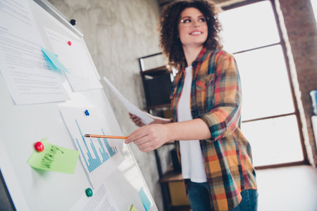 Young professional woman analyzing data in a modern office setting with casual style and a checkered shirtの写真素材