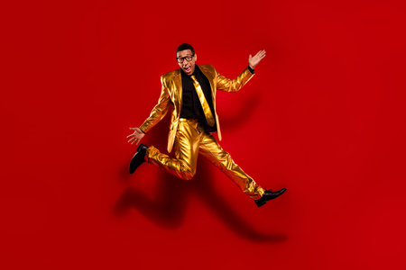 Energetic young man in a stylish gold suit jumping against a vibrant red background, exuding charm and elegance.の写真素材