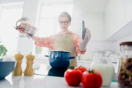 Elderly woman in kitchen cooking with enjoyment as she wears an apron and explores homemade recipes with fresh ingredientsの写真素材