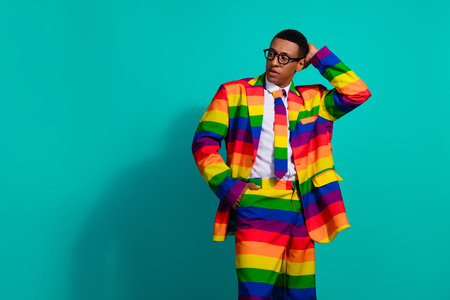 Stylish young man in a colorful rainbow suit standing confidently against a vibrant turquoise background.の写真素材