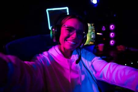 Photo of cute lovely blonde girl take selfie photo play gamer computer game late night blue purple indoors house late neon lightの写真素材