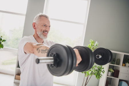 Elderly man lifting weights in a bright home gym showcasing active lifestyle and physical fitness commitmentの写真素材