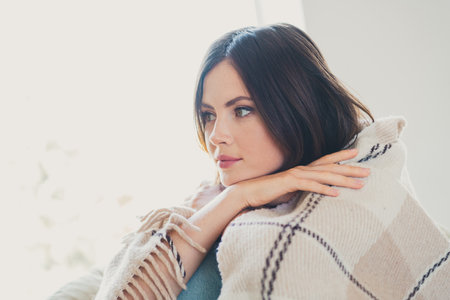 Charming young woman with bob hairstyle relaxing indoors under a cozy blanketの写真素材