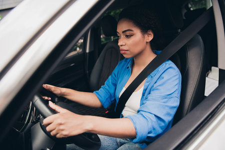 Young woman confidently driving car through city streets on sunny day
