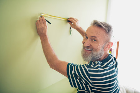 Elderly man enjoying a relaxing weekend at home, measuring wall for a new projectの写真素材