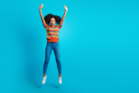 Photo of crazy energetic jumping raised hands up girl wavy hair wear casual jeans and striped t shirt isolated on blue color backgroundの写真素材