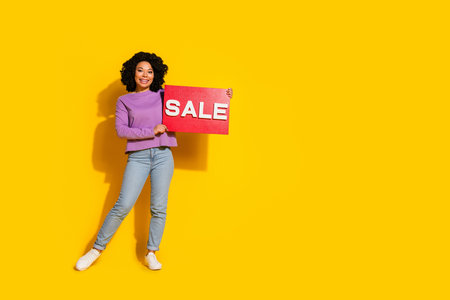 Full length photo of pretty young woman hold sale poster empty space isolated on yellow color backgroundの写真素材
