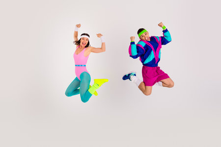 Energetic young couple in retro sportswear jumping in excitement against a white backgroundの写真素材