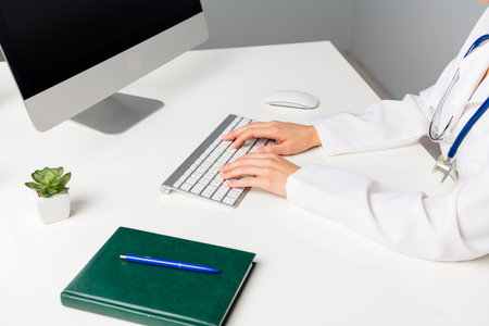 Doctor at work typing on a computer keyboard in a modern medical officeの写真素材