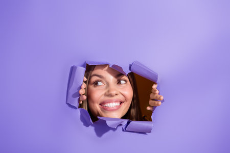 Photo portrait of attractive young woman interested look face toothy smile tear purple paper color backgroundの写真素材