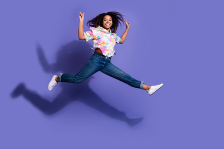 Energetic young woman with vibrant black curls leaps joyfully in front of a vivid purple backdrop in...