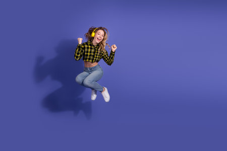 Energetic young woman jumping joyfully in front of a purple background, expressing excitement and leisureの写真素材