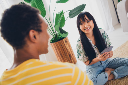 Photo of lovely cheerful couple friends sit floor play poker game hold cards indoors apartmentの写真素材