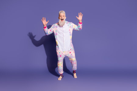 Joyful man in colorful unicorn onesie posing playfully against a vibrant purple backgroundの写真素材