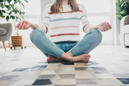 Young woman meditating in a cozy living room, enjoying relaxation and tranquility during her weekend break at home in natural daylight.の写真素材