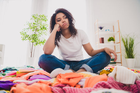 Young woman sitting among colorful clothes for donation in a bright living roomの写真素材
