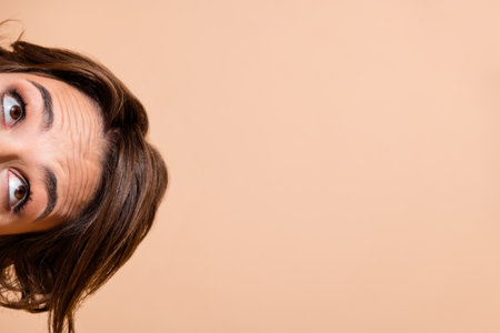 Cropped photo portrait of attractive young woman look empty space hide face isolated on beige color backgroundの写真素材