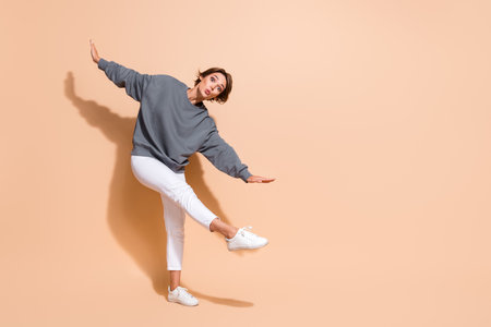 Full length photo of funny girlish girl wear pullover white trousers hold arms like wings pouted lips isolated on beige color backgroundの写真素材